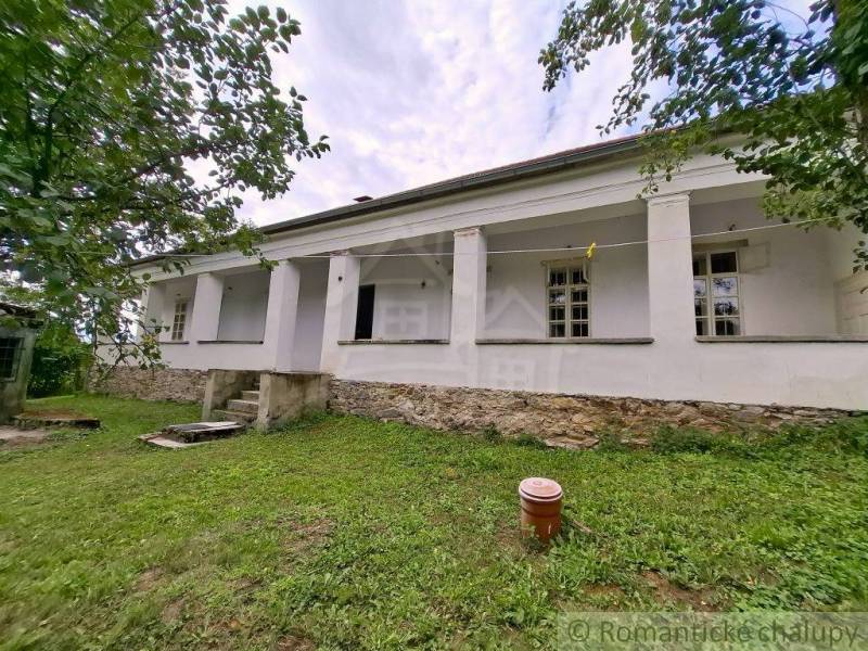 A family house in Dobroč, white facade, stone foundation, surrounded by greenery and trees.