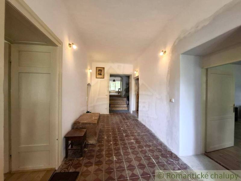 A hallway in a family house with patterned tiles, bright, wooden doors, paintings on the wall.