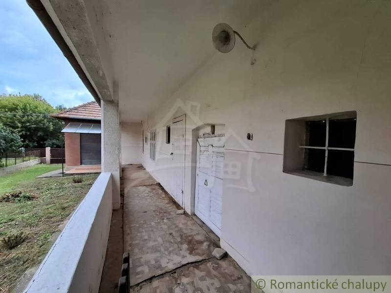 The veranda of a family house in Mužla with a white facade and a grassy yard.