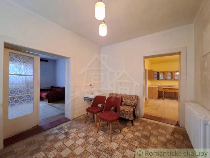 Interior of a family house with armchairs, a sink, a kitchen, and two open doors.