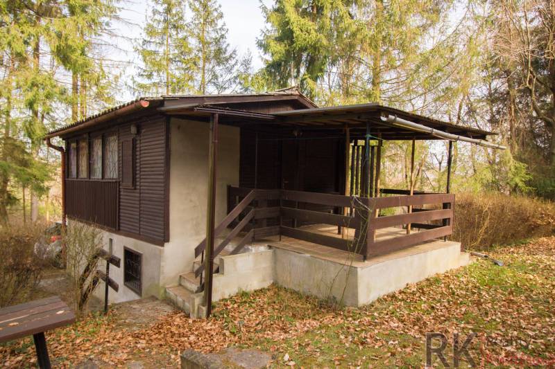 A wooden cabin on recreational land in Holčíkovce, surrounded by trees and fallen leaves.