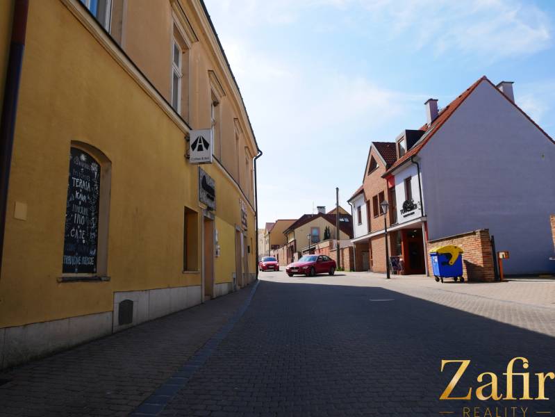 A street in Trnava with dining spaces, yellow and brick buildings, parked car.