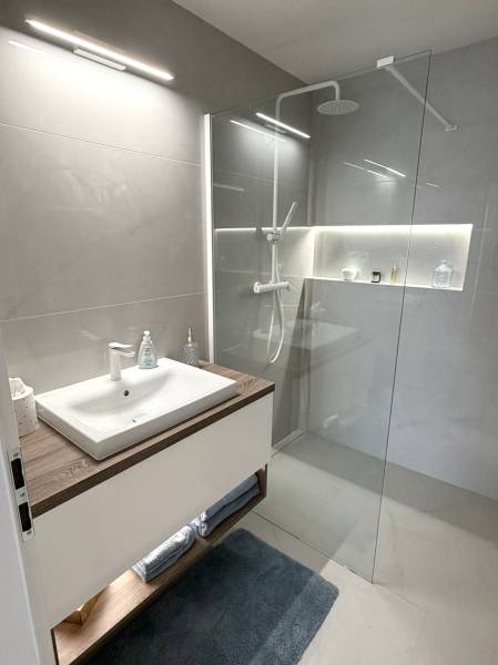 Bathroom with a sink, glass shower enclosure, and light tiles in a 2-room apartment.
