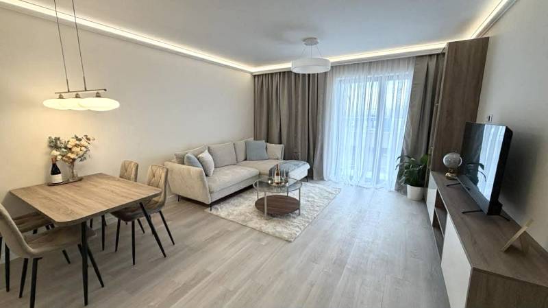 Living room in a two-room apartment with a wooden decor floor, a sofa, and a dining table.