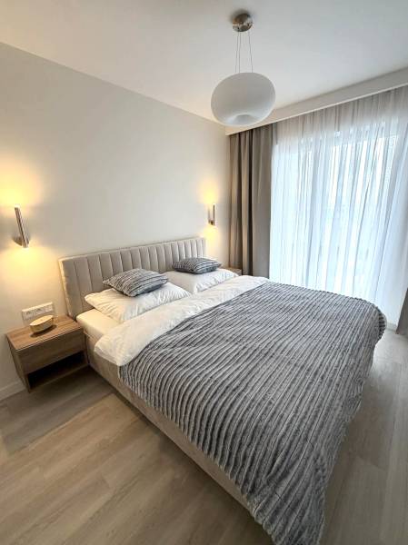 Bedroom in a two-room apartment with wood-patterned flooring, a bed, and curtains.