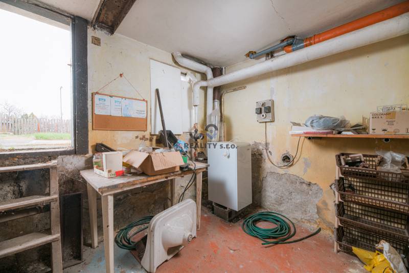 Basement of a family house with a boiler, shelves, hose, and work table.