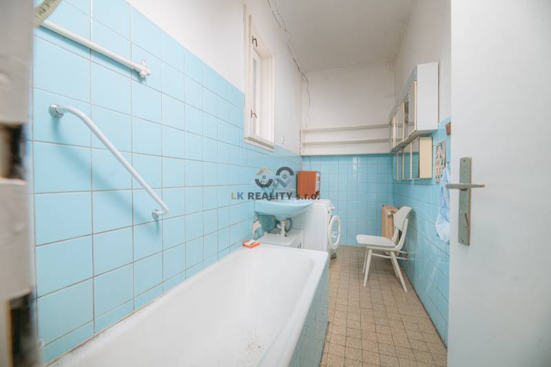 Bathroom with blue tiles, sink, bathtub, washing machine, and shelves in a family house.