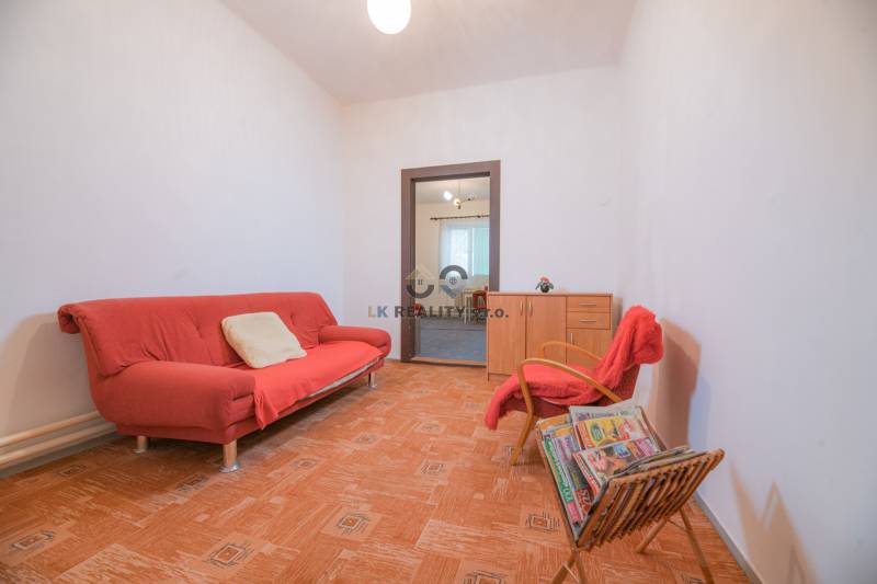 Living room with a red sofa, armchair, magazines, and wood-patterned flooring in a family house.