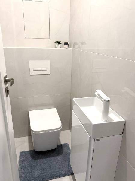 A toilet with a sink in a 2-room apartment, light tiles and a blue carpet.