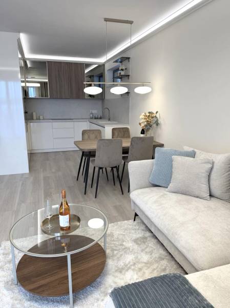 Living room in a two-room apartment with a wooden decor floor, sofa, and dining table.