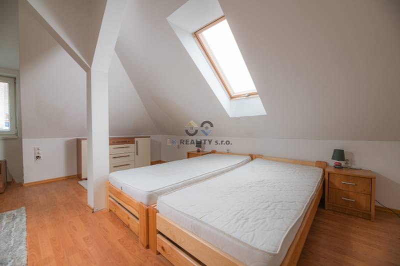 Attic bedroom with two single beds and a wooden decor floor in a 2-room apartment.