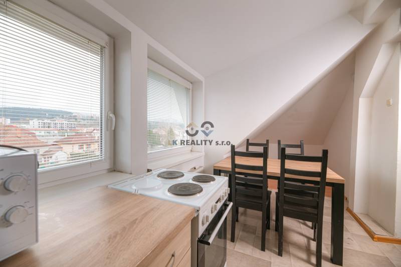 A kitchen in a 2-room apartment with a stove, microwave, and dining table, with a view of the city.