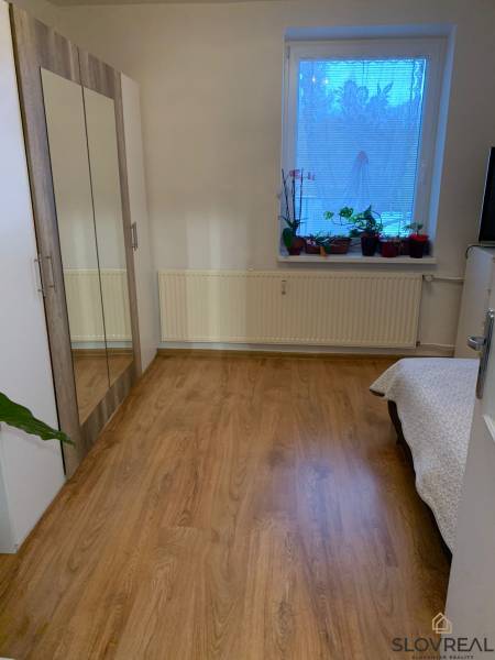 A room in a 2-room apartment with a wooden decor floor and a wardrobe with a mirror.
