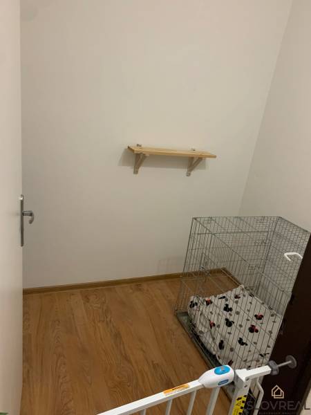 A small room with a wall shelf, a floor with a wooden decor, and a cage for an animal.