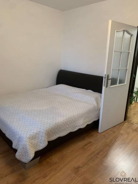 Bedroom in a 2-room apartment with a wood-patterned floor and a large bed.