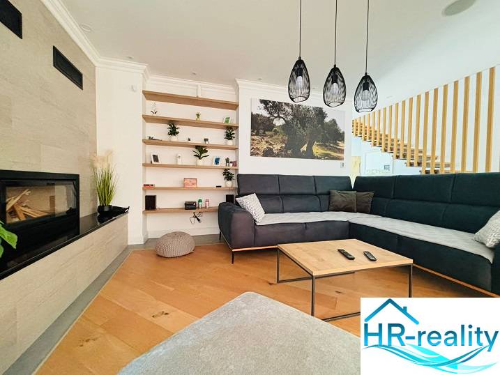 Interior of a villa with a wooden decor floor, a comfortable sofa, and a built-in fireplace.