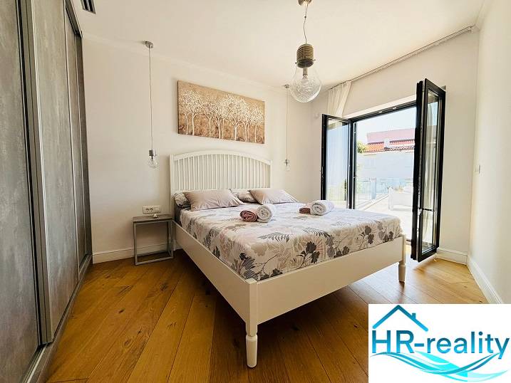 A bright bedroom in a villa with a bed, balcony, and wooden decor flooring.