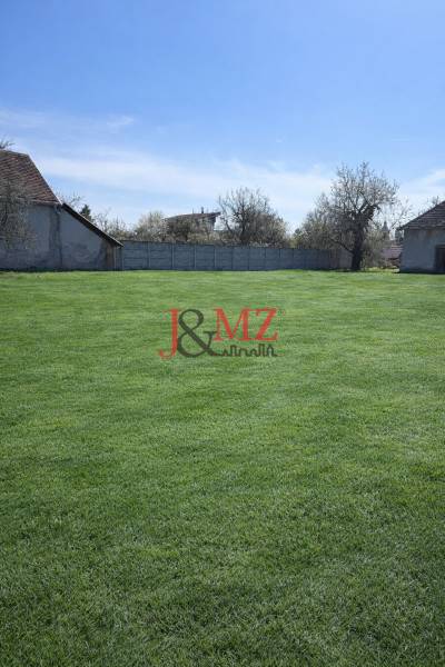 A garden in Dolná Seč surrounded by family houses and fencing under a blue sky.