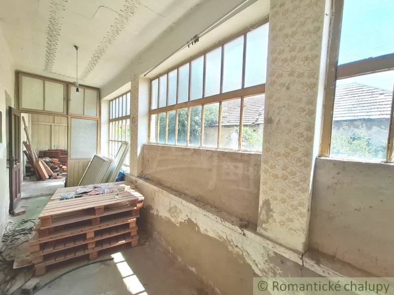 A cottage with a spacious veranda, large windows, and a variety of stored materials.