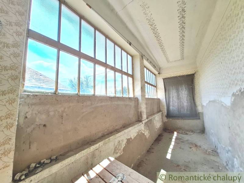 A cottage in Kamenný Most with a long veranda and large windows, in need of renovation.