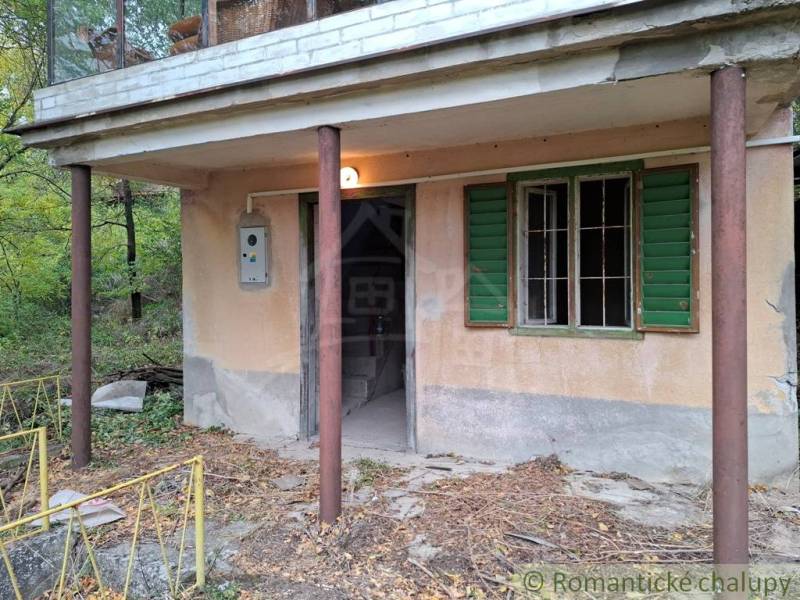A cottage in Kamenín with a veranda and green shutters surrounded by nature.