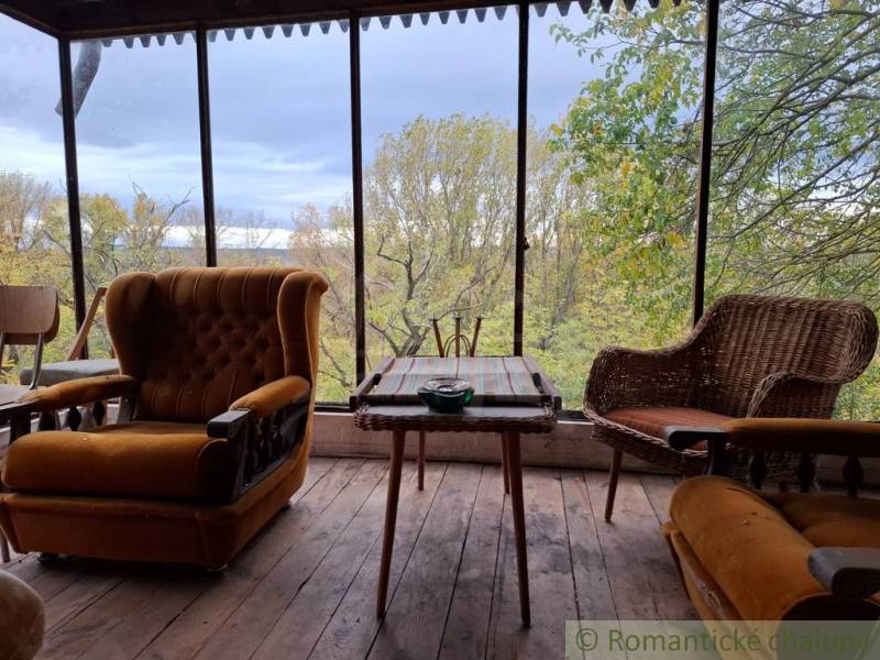 A cottage with seating featuring antique chairs and a view of the autumn forest.