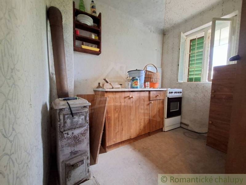 The interior of a cottage with a simple kitchen unit, a stove, and an open window.