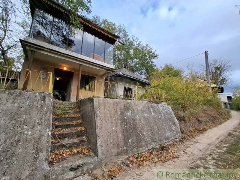 A cottage in Kamenín surrounded by greenery, with large windows and a concrete front entrance.