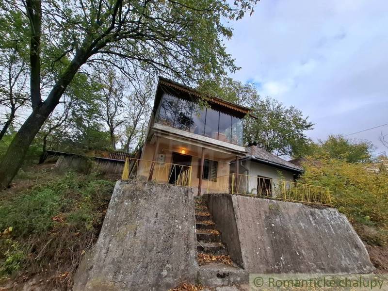 A cottage in Kamenín with a concrete foundation and large windows amidst trees.