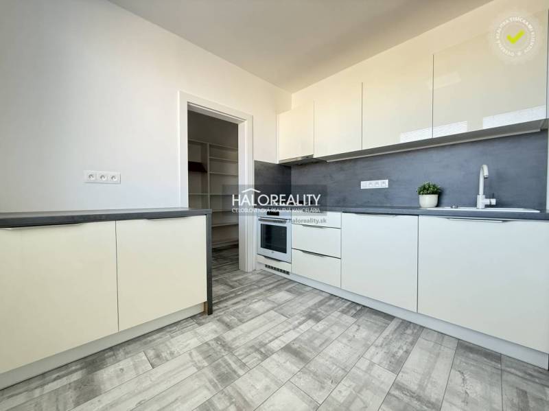 A kitchen in a 2-room apartment with a grey floor featuring a wooden design and white cabinets.