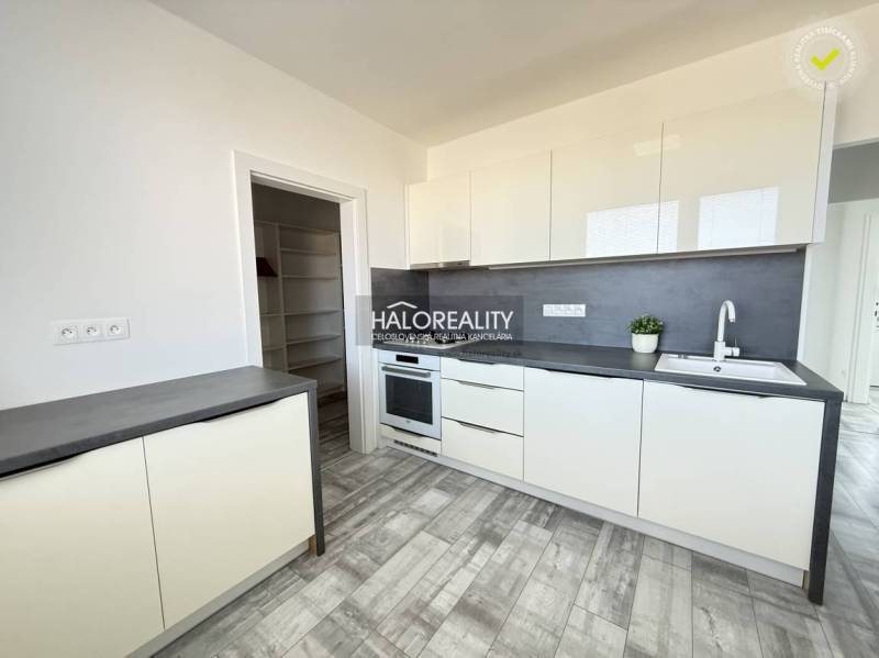 A kitchen in a 2-room apartment with white furniture and a wooden decor floor.