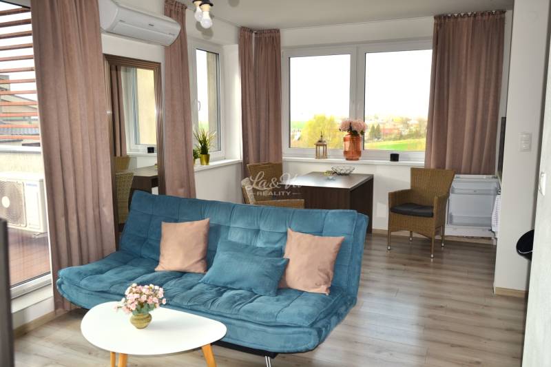 Living room with a sofa, table, plants, and a wooden-patterned floor in a two-room apartment.