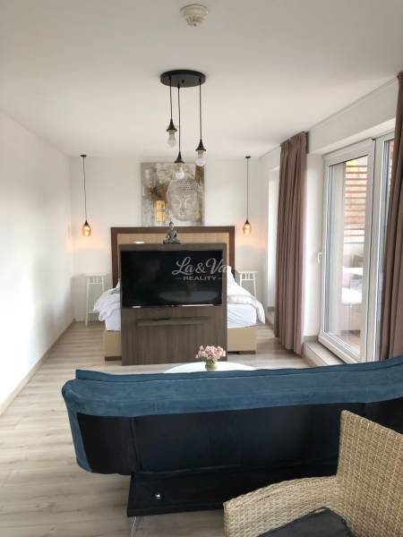 Living room in a two-room apartment with a wooden decor floor and a separate bedroom area.
