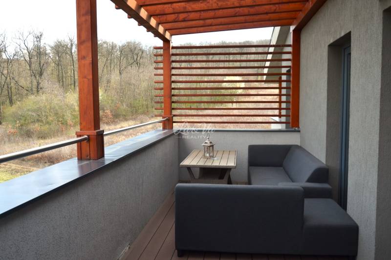 A balcony of a 2-room apartment with wooden decor and a view of greenery.