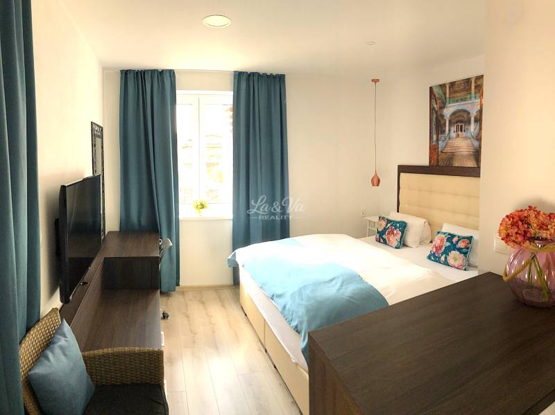 A bright room in a 2-room apartment with blue curtains and a wooden decor floor.