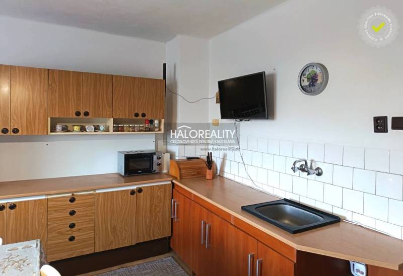 A kitchen in a family house with a wooden kitchen unit, a microwave, and a television on the wall.