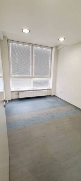 A room with large windows, a wooden decor floor, and a radiator in the office.