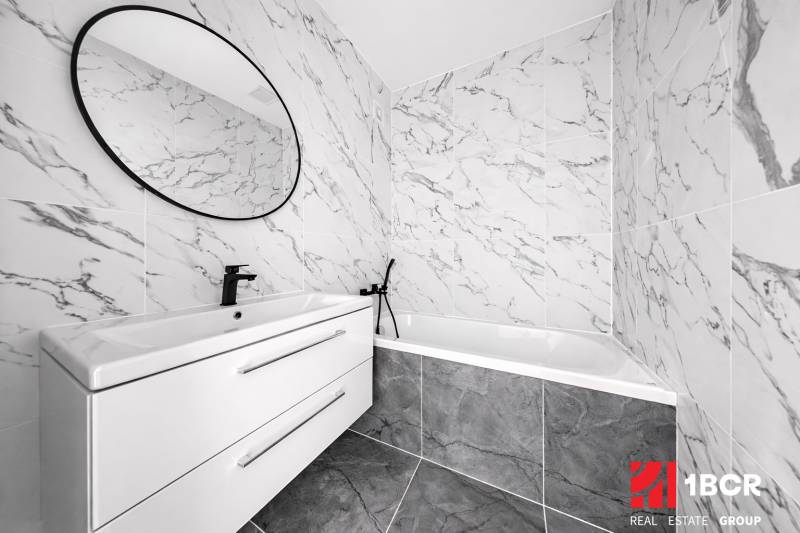 A bathroom with marble tiles, an oval mirror, and a modern sink in a 3-room apartment.