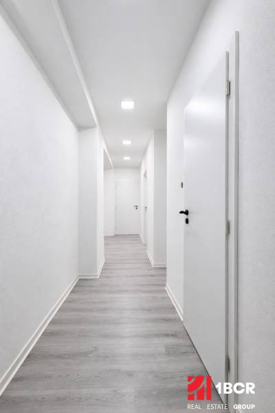 A hallway with white walls and a wooden decor floor in a 3-room apartment.