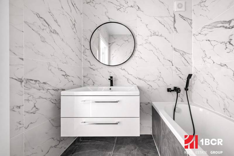 A bathroom in a 3-room apartment with marble tiles, a sink, and a mirror.
