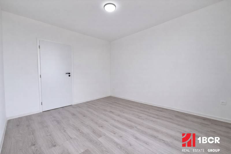 An empty room in a 3-room apartment with wood-patterned flooring and white walls.