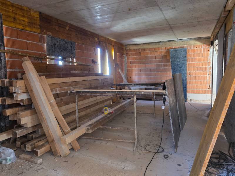 Construction site of a 3-room apartment with unfinished brick walls and wooden beams.