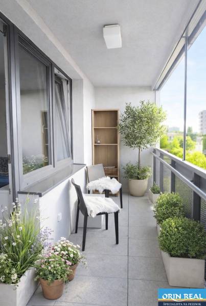 A balcony of a 2-room apartment with plants and two chairs, view of greenery.