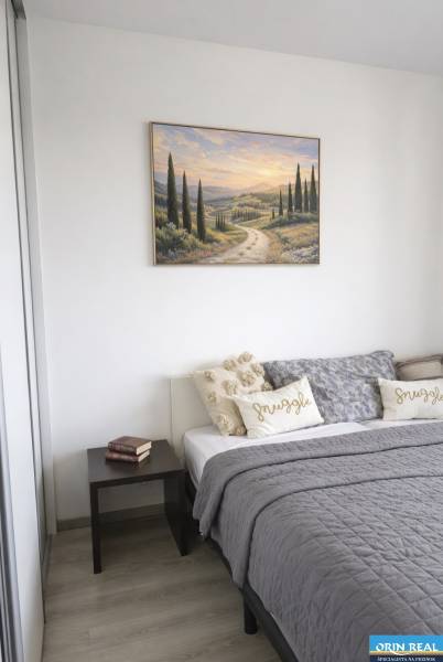 Bedroom in a 2-room apartment with a bed, a painting, and a table on a floor with a wooden decor.