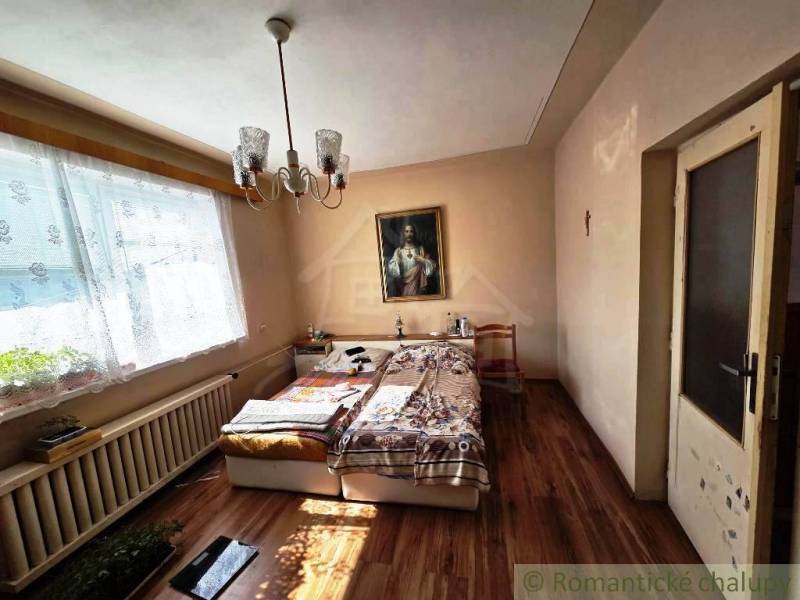 Bedroom in a family house with a bed, chandelier, painting, and floor with wooden decor.