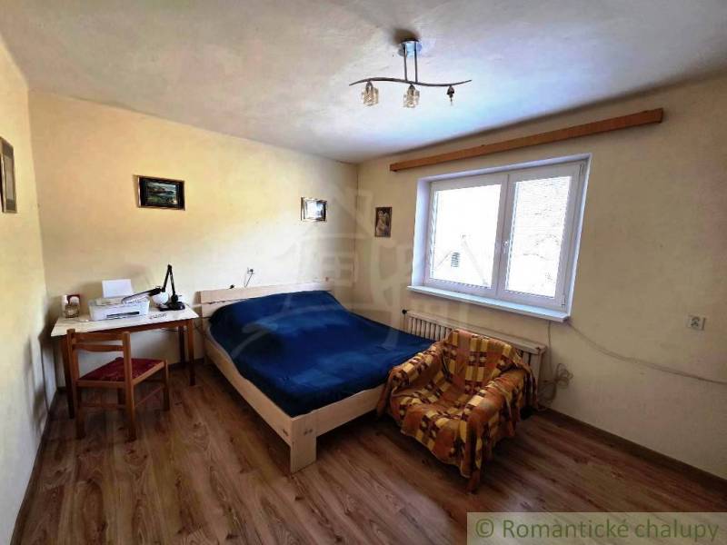 A bedroom with a bed, table, and chair in a family house. The floor has a wooden decor.