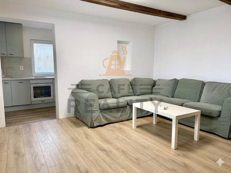 Living room with a corner sofa, wood-patterned flooring, and a kitchen in a family house.