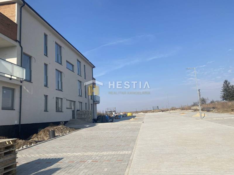 A newly built 3-room apartment in Petrová Ves with a surrounding paved road and clear sky.
