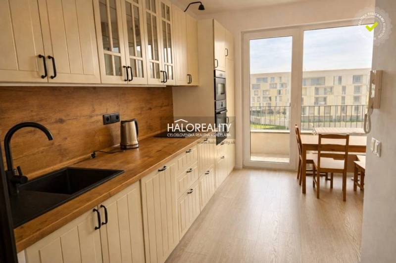 A kitchen with a wood-patterned floor, white cabinets, and a dining table in a two-room apartment.
