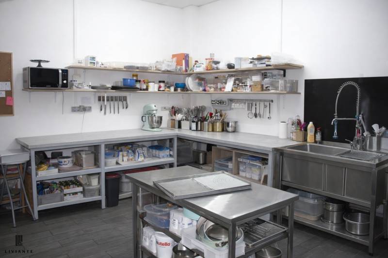 Professional kitchen with stainless steel surfaces, shelves, and kitchen equipment, floor with wooden decor.